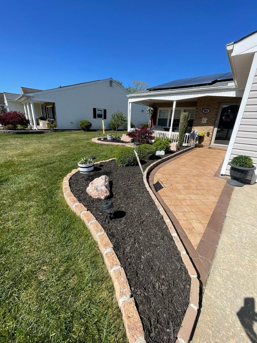 Curved mulch bed with stone edging beside a paver walk